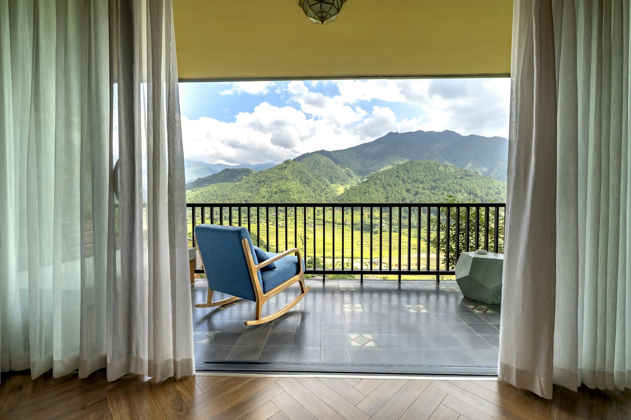 Inviting balcony with a scenic mountain view, featuring a blue chair and sheer curtains.